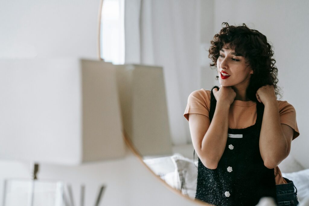 Adult dreamy female with black outfit looking away in front of mirror at home